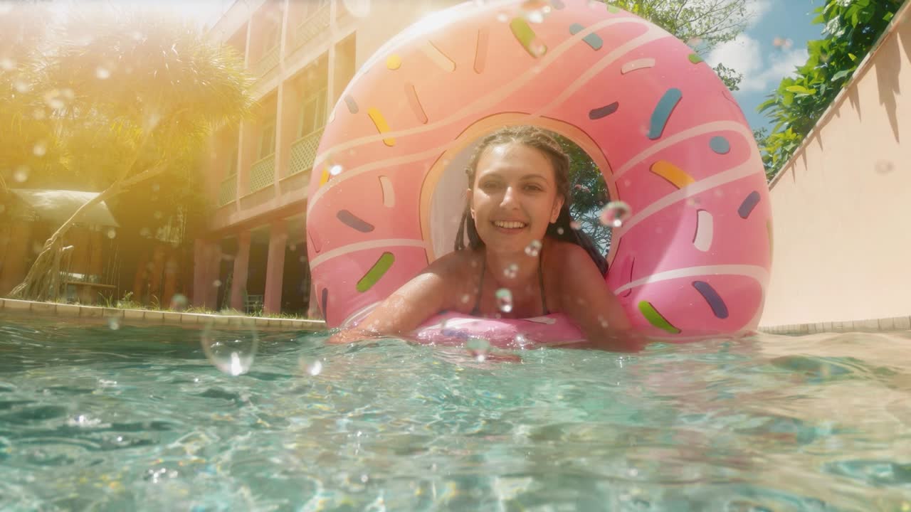 mujer con gafas de sol en bikini azul acostado en rosado inflable donut flotan en la piscina en un día soleado de verano. mira a la cámara. mujer bikini piscina en anillo de goma de sandía vacaciones relajantes