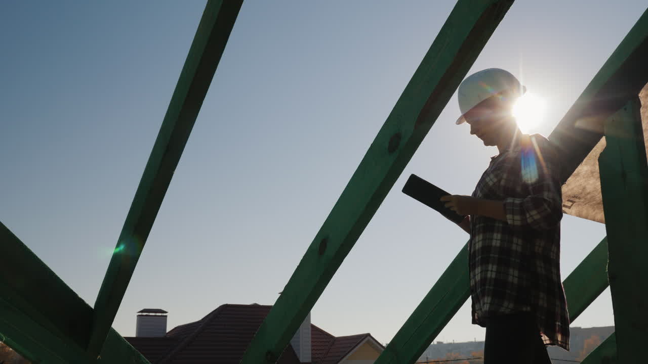 el ingeniero trabaja con una tableta en el techo de la cabaña controla la calidad del trabajo de construcción