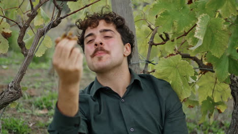 Closeup-winegrower-tasting-grapes-sitting-under-vine-bush.-Farmer-enjoy-harvest.