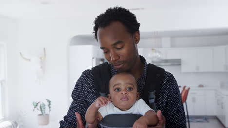 portrait of father playing game with smiling baby son in sling at home