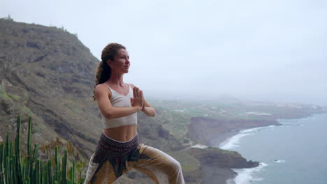 En-Una-Costa-Rocosa-Durante-La-Puesta-De-Sol,-Una-Joven-Practica-Yoga,-Destacando-Un-Estilo-De-Vida-Saludable,-La-Armonía-Y-La-Unidad-De-Los-Humanos-Y-La-Naturaleza-Con-El-Telón-De-Fondo-Del-Océano-Azul.