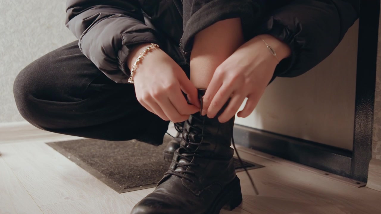 Hands tie boots. Closeup of hands securing old black footwear. Intimate scene of tying aged leather boots at doorway. Closeup image capturing hands preparing worn black footwear before leaving