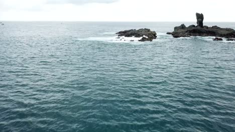 aerial 4k fishing boat cruising past large rock formations in ocean, indonesia