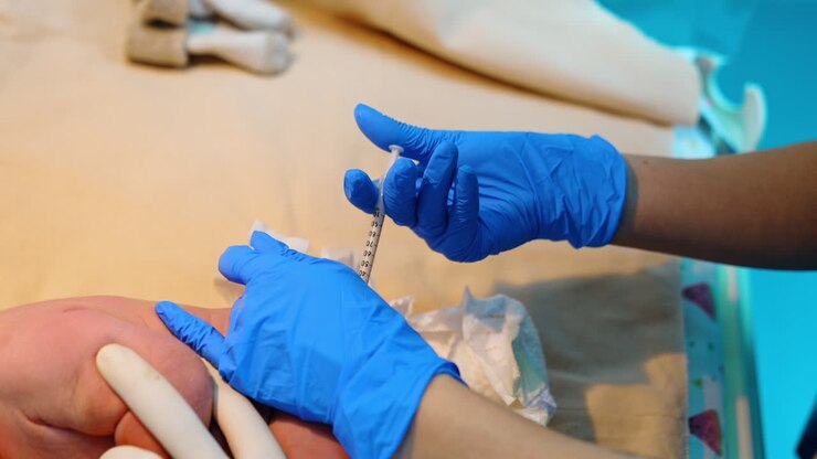 Medic wearing blue latex gloves give a shot to a newborn child. Injection right after birth. Close up.