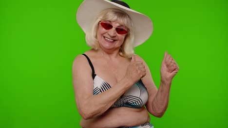 Elderly-woman-tourist-in-swimsuit-and-sunglasses,-looking-at-camera,-smiling,-showing-thumbs-up