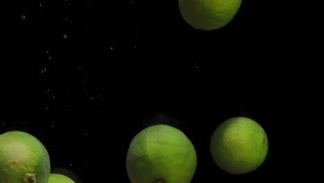 fresh limes falling into the water with air bubbles.