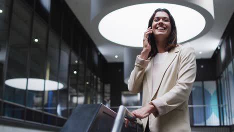 smiling caucasian businesswoman using smartphone in lobby of modern office