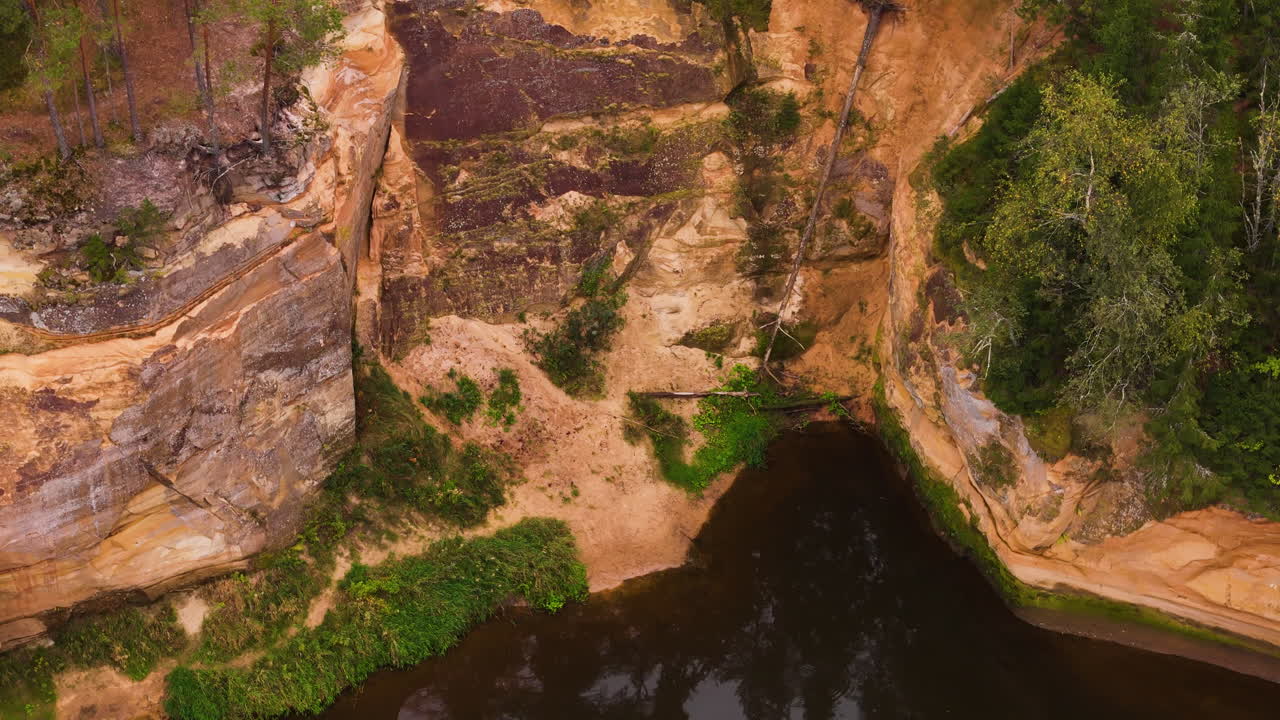 Aerial footage of Erglu Cliffs with sandstone layers by a calm river in Latvia.