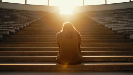 person sitting alone on large steps into the light at sunset