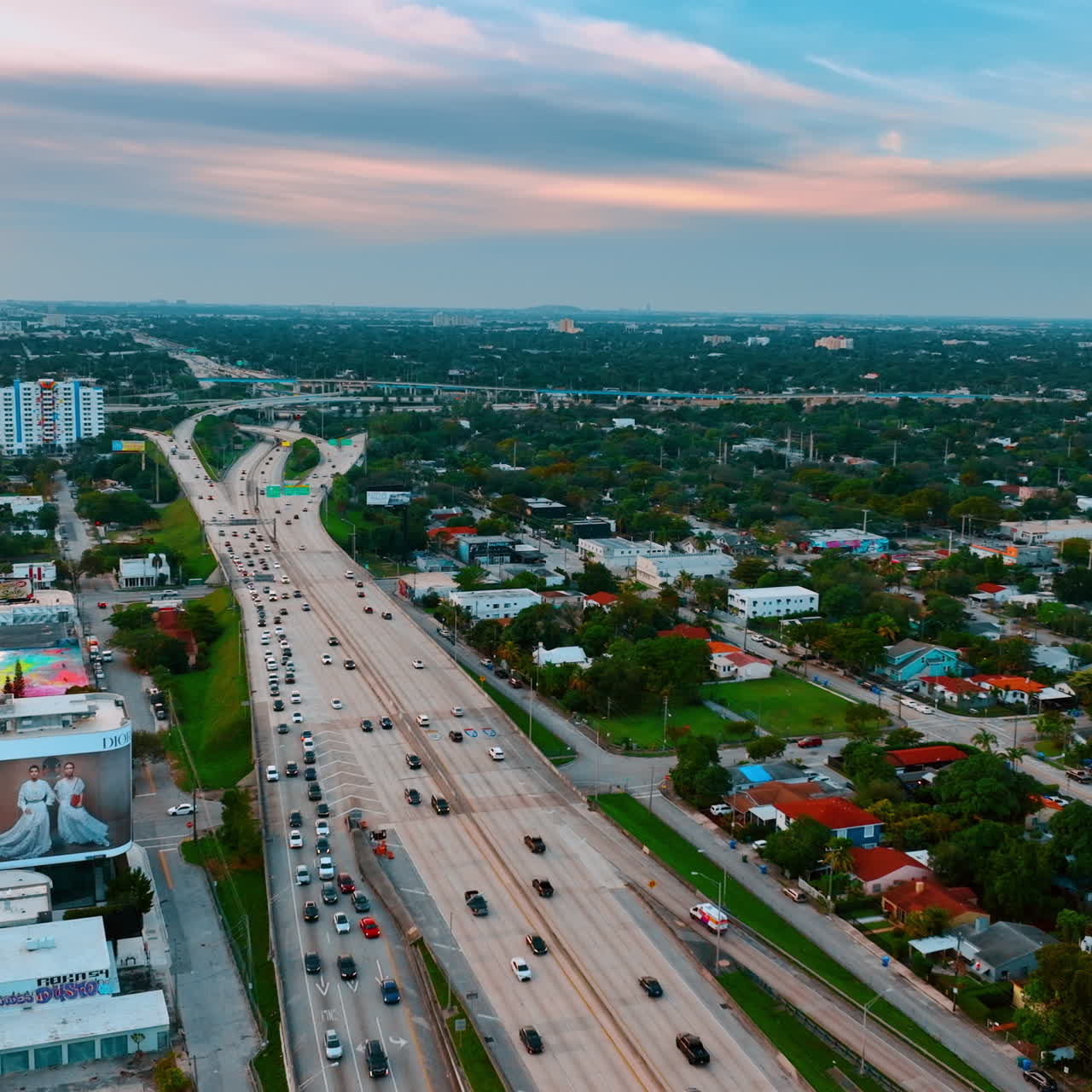 Going up above the highway with multiple vehicles driving by. Panoramic view of the low rise urban area in Miami, Florida, USA.