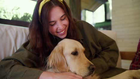 toma de primer plano: una chica morena con una venda amarilla en la cabeza con una chaqueta verde acaricia a un perro de color claro en un gazebo en la naturaleza