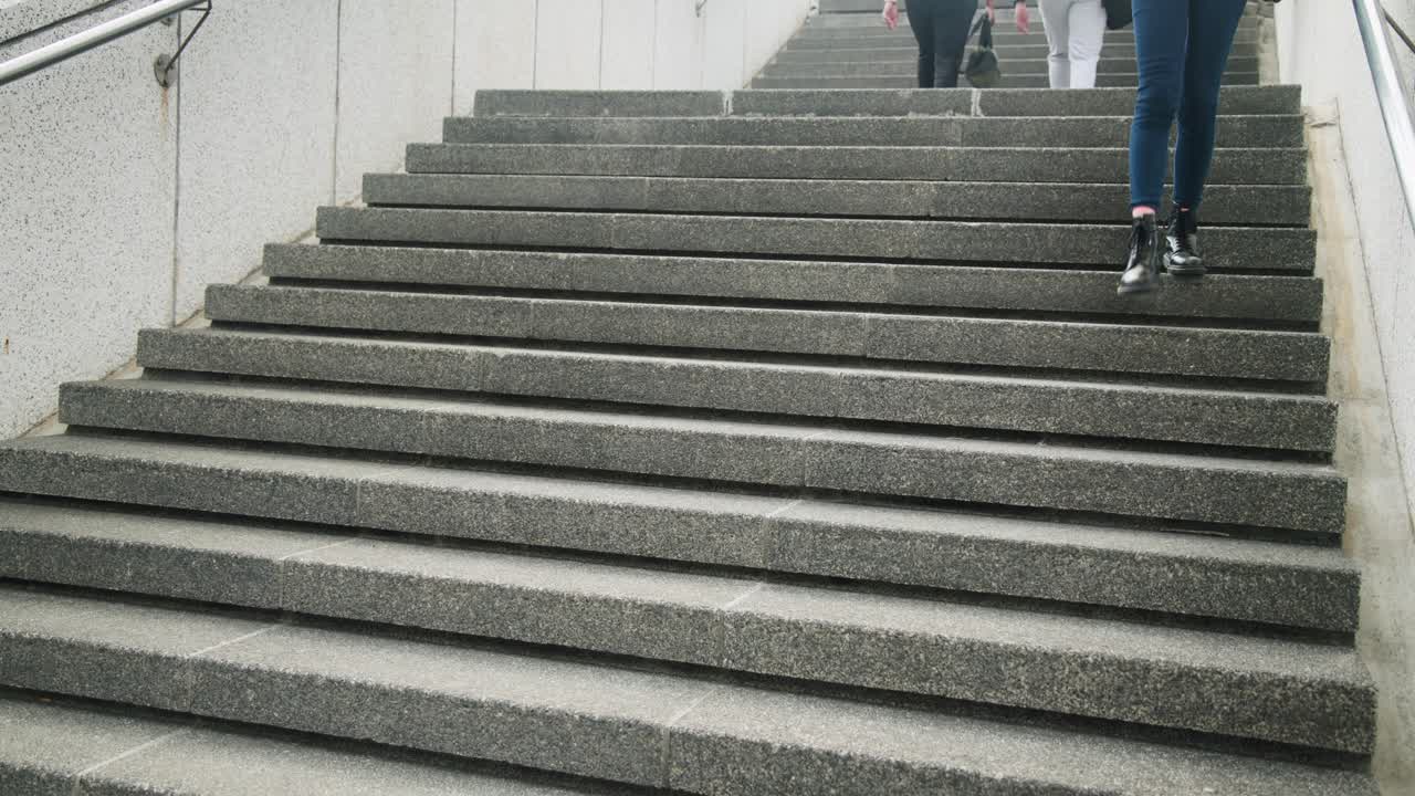 Two women entering frame with duffel, shoulder bag in sneakers climbing concrete stairs to street
