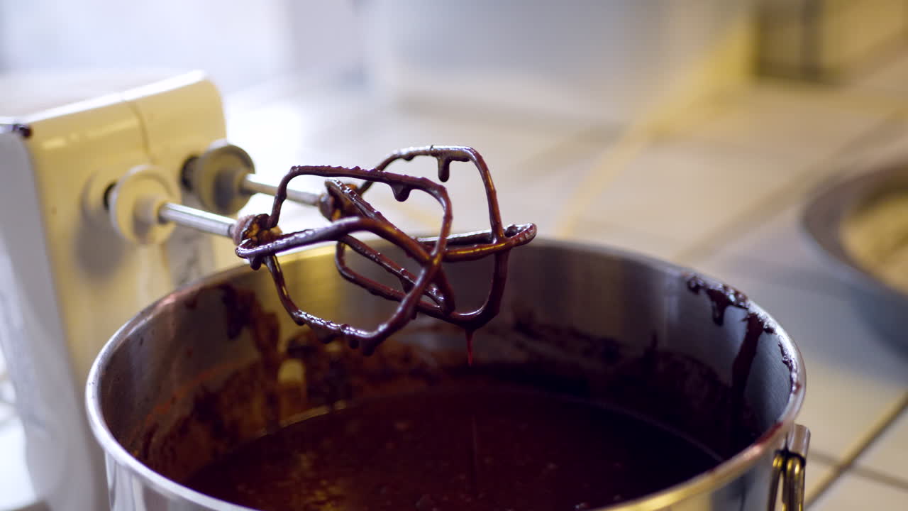 Delicious vegan chocolate cake batter dripping from electric mixer into a bowl while baking in the kitchen SLIDE RIGHT