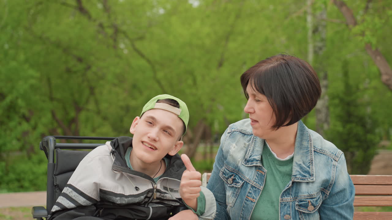 Joyful Supportive Interaction, Woman Shows Support And Cheerfulness To Smiling Teenager In Wheelchair, Vibrant Scene Of Woman Encouraging Teen In Wheelchair With Thumbs Up And Friendly Gestures