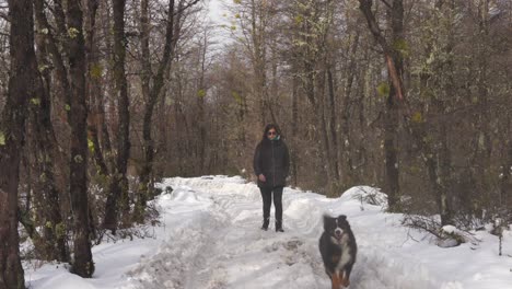 Woman-and-dog-walking-along-a-snowy-path-in-a-forest-in-Patagonia,-towards-the-camera