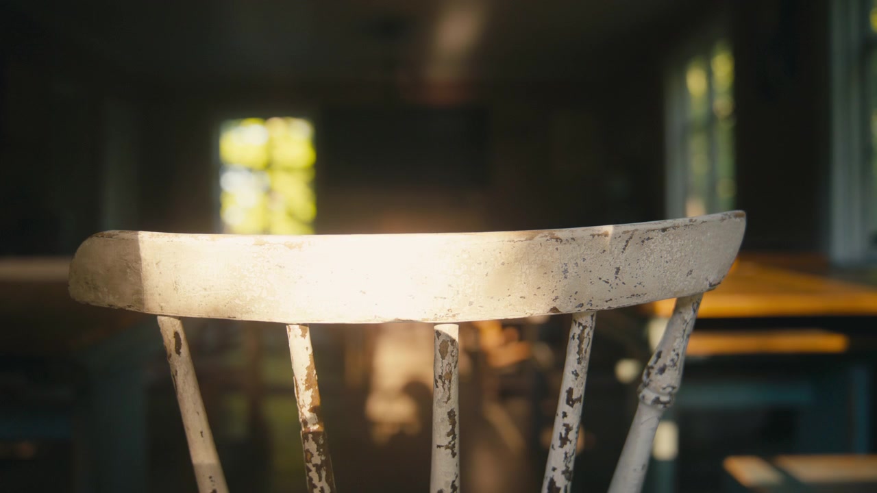 La calda luce del sole accarezza dolcemente lo schienale usurato di una vecchia sedia di legno in un'aula storica, creando una scena nostalgica piena di ricordi, quiete e un carattere senza tempo.