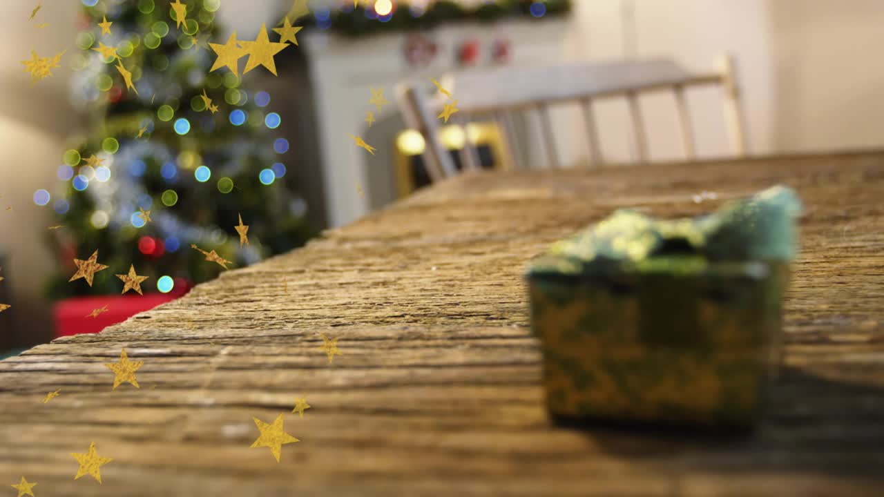 Confetti starting edge drifting over table toward gift box beside lit tree, creating holiday warmth