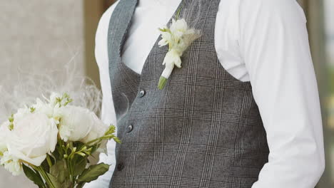 elegant young man in grey vest with boutonniere and flowers