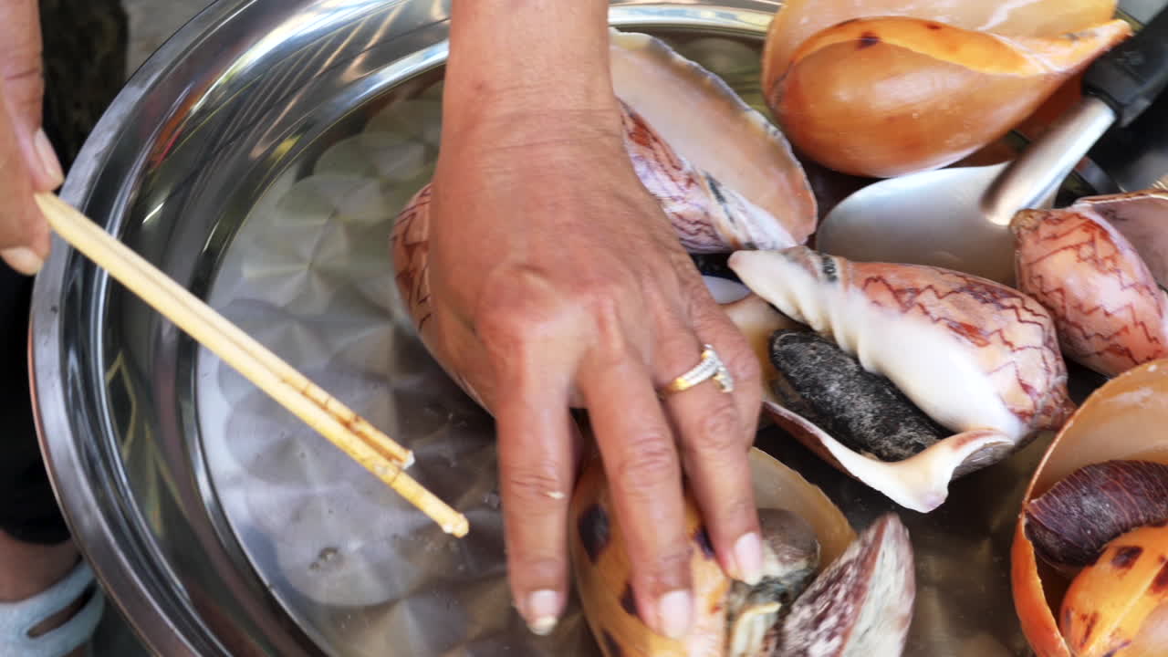 사람은 젓가락으로 껍질에서 신선한 바다 달팽이를 골라낼 준비를 합니다