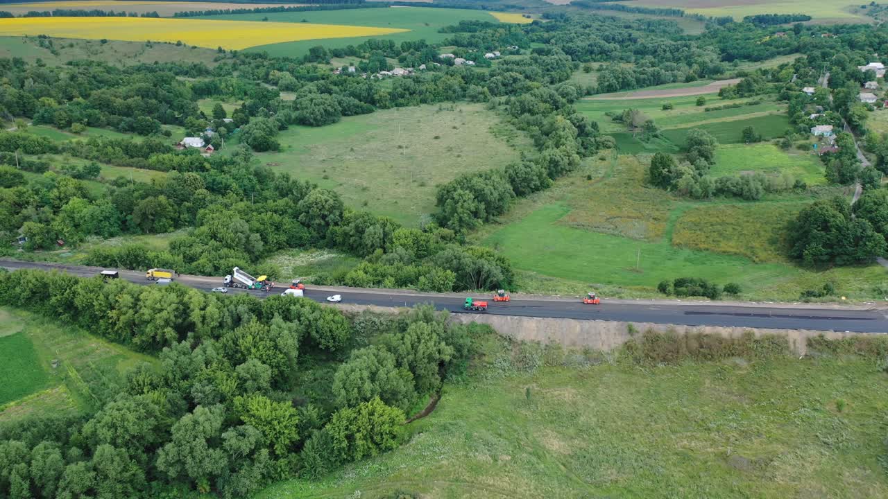 Aerial view of the road among nature. Side view of the highway with cars surrounded by green fields and forests. Machinery on the road during roadworks.