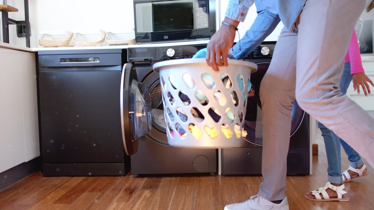 African American man carrying basket, loading washer for washing, youth female watching, copy space
