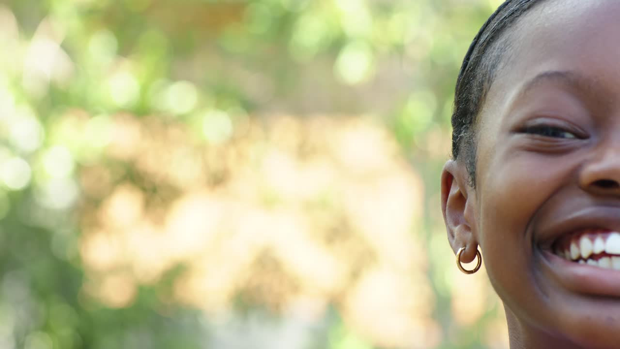 Ragazza afroamericana inquadrata in movimento, sorride e ride mostrando un orecchino d'oro in giardino, con spazio per il testo.