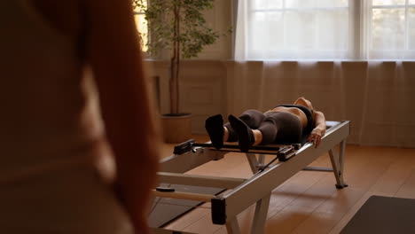 woman exercising on a pilates reformer machine with an instructor