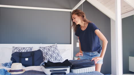 Mujer-Intentando-Cerrar-La-Maleta-De-Vacaciones-Completa-En-El-Dormitorio