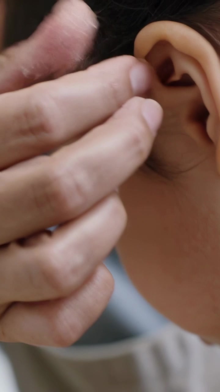 Video verticale: Adulto in grembiule che si china per aggiustare l'orecchino a un bambino al tavolo prima di imboccarlo con un cucchiaio.