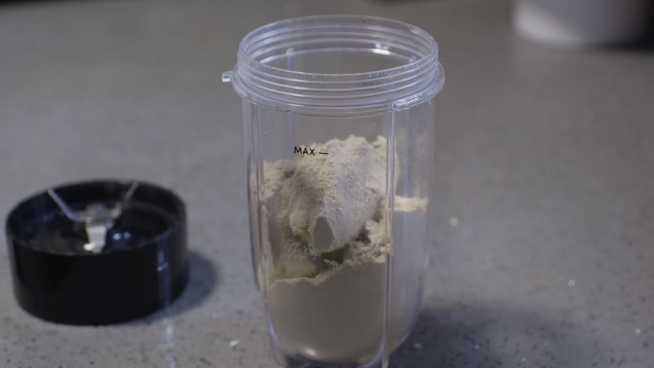 Preparazione di un frullato proteico. Versare il latte in un bicchiere da frullatore con banana e proteine in polvere.