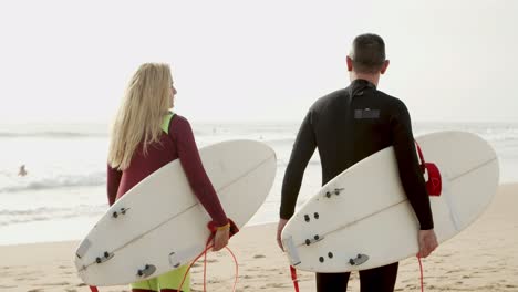 back view of couple with surfboards walking on beach