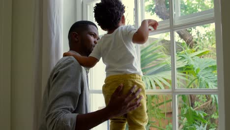 Seitenansicht-Eines-Jungen-Schwarzen-Vaters,-Der-Mit-Seinem-Sohn-Auf-Der-Fensterbank-In-Einem-Komfortablen-Zuhause-Spielt,-4K