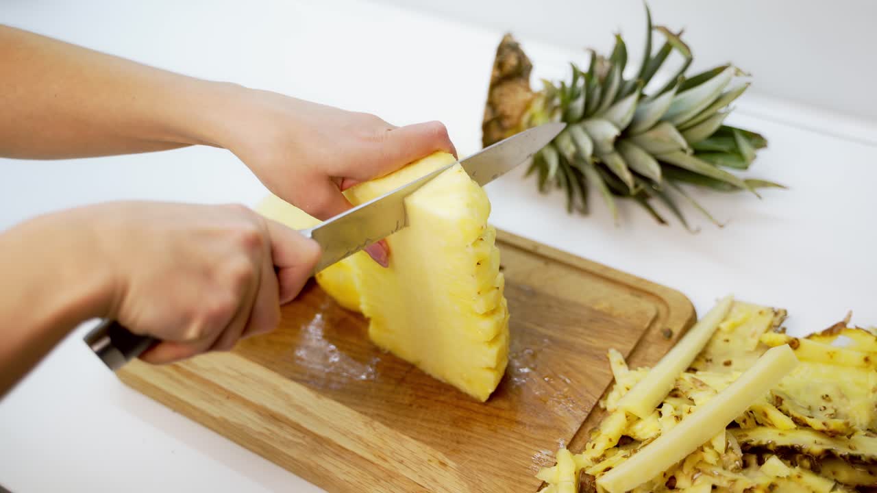 Woman cutting pineapple. Fresh pineapple on the cutting board. Hands of a female preparing exotic fruit for guests. Close-up.