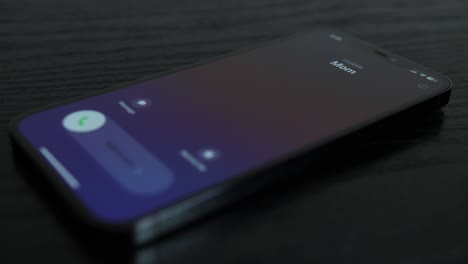 Close-up-shot-of-an-iPhone-receiving-a-call-from-Mom-on-black-wooden-table