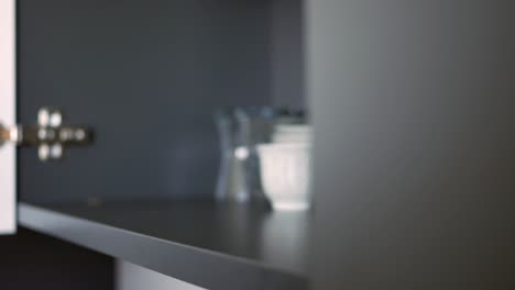 hand holding a small decorative cup on a kitchen shelf