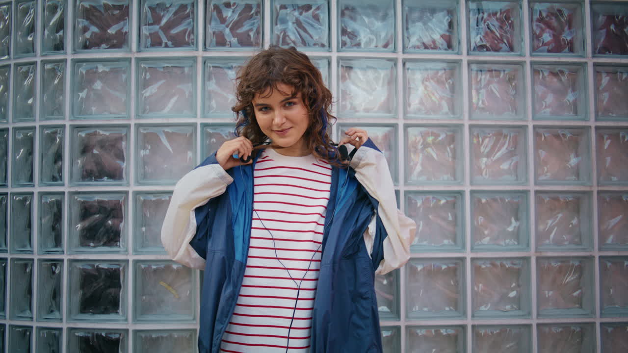 adolescente poniéndose auriculares posando en el edificio de pared de vidrio de cerca. chica feliz