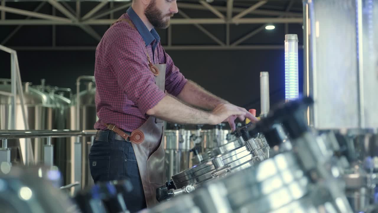 un joven cervecero con un delantal de cuero supervisa el proceso de fermentación de la cerveza en una fábrica de cerveza moderna