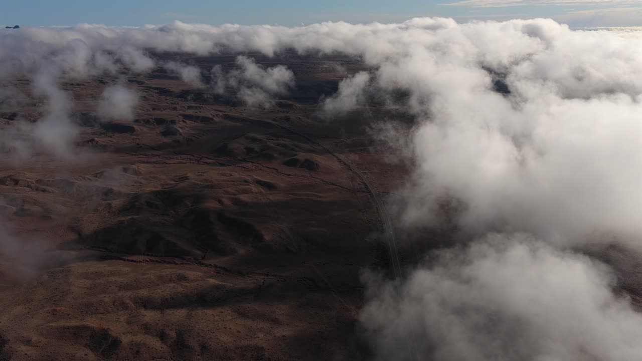 En filmisk droneudsigt af en bil, der navigerer på en ensom vej i et fjerntliggende badlands-område. Morgenstågen og den dramatiske skybevægelse over ørkenbakkerne skaber et perfekt etableringsskud.
