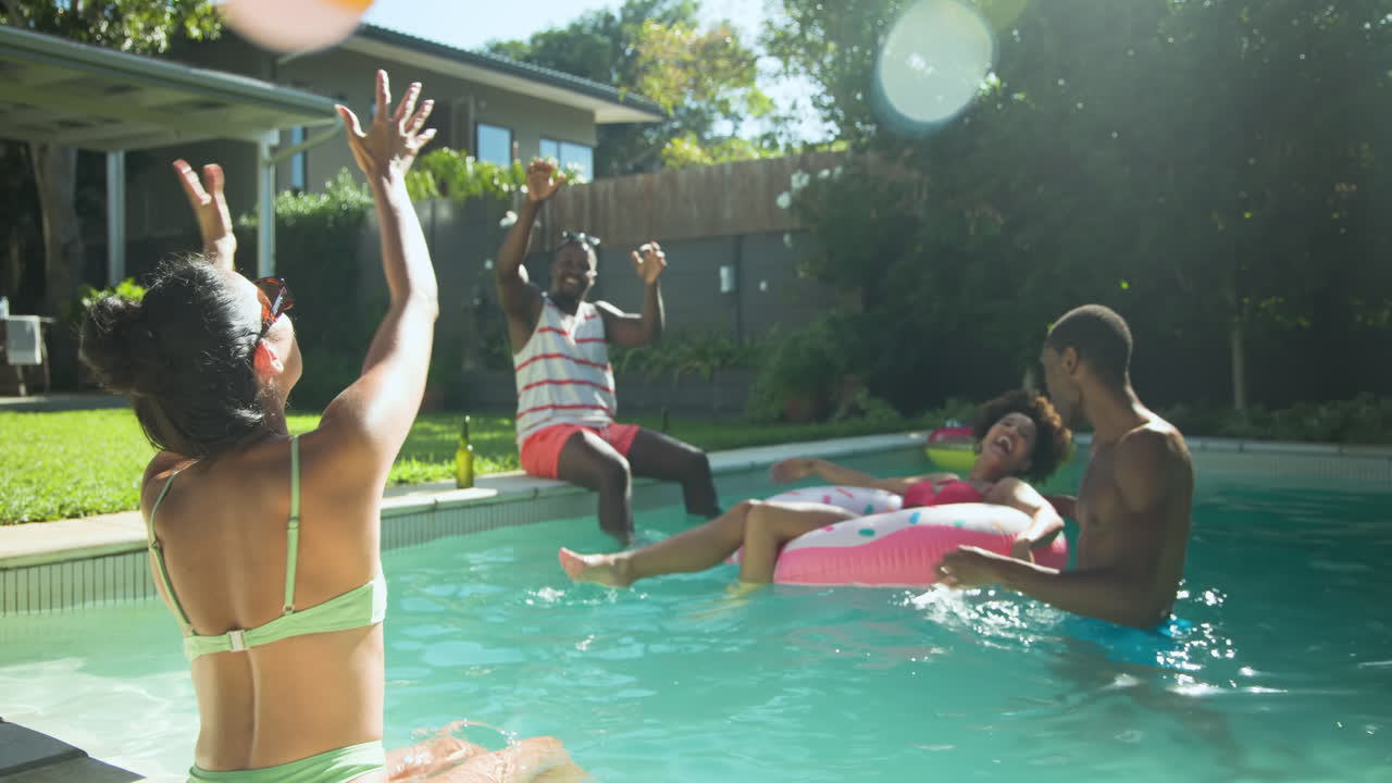 Diverse friends enjoying sunny day playing with beach ball in backyard swimming pool