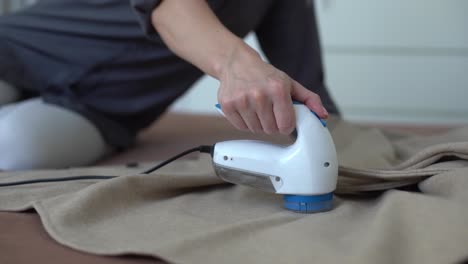 wireless device for cleaning knitted fabrics from lint. the woman is removing the lint from the sweater.