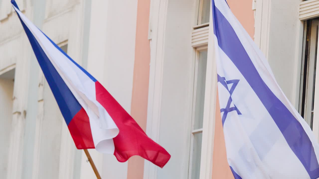 Czech and Israeli flags wave on building facade in daylight, gentle wind, urban setting