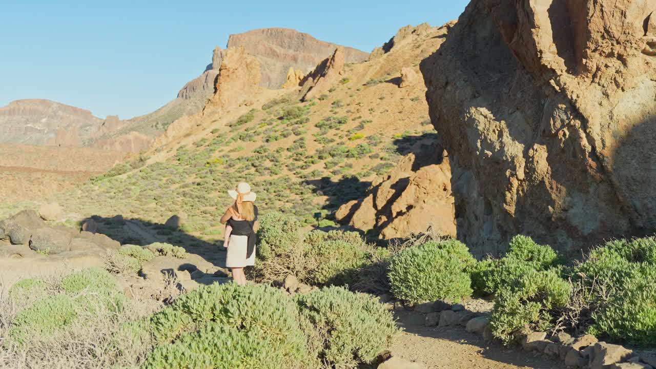 어린 어머니가 손에 아이를 들고 테네리페의 언덕 풍경에서 고 있습니다.