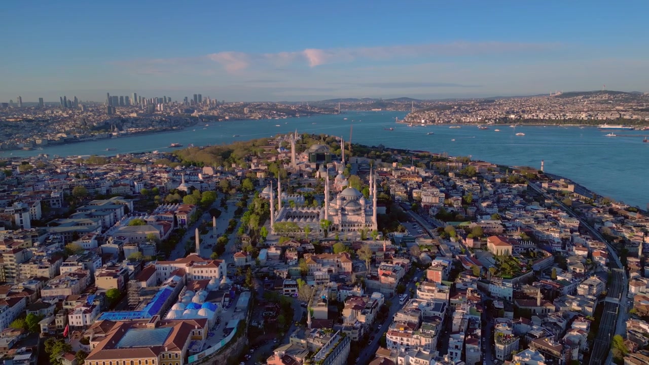 Mavi Cami olarak bilinen Sultan Ahmet Camii, berrak bir gökyüzüne karşı İstanbul şehir manzarası ve Boğaz ile belirgin bir şekilde duruyor. Geriye doğru uçan akıcı bir havadan drone panoraması.