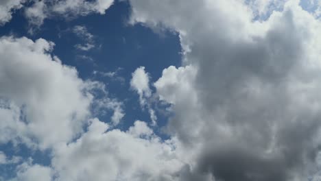 Nubes-Blancas-Formándose-Y-Quemándose-A-La-Luz-Del-Sol-Contra-El-Cielo-Azul-Con-Algunas-Nubes-Grises-Pesadas-En-Desarrollo