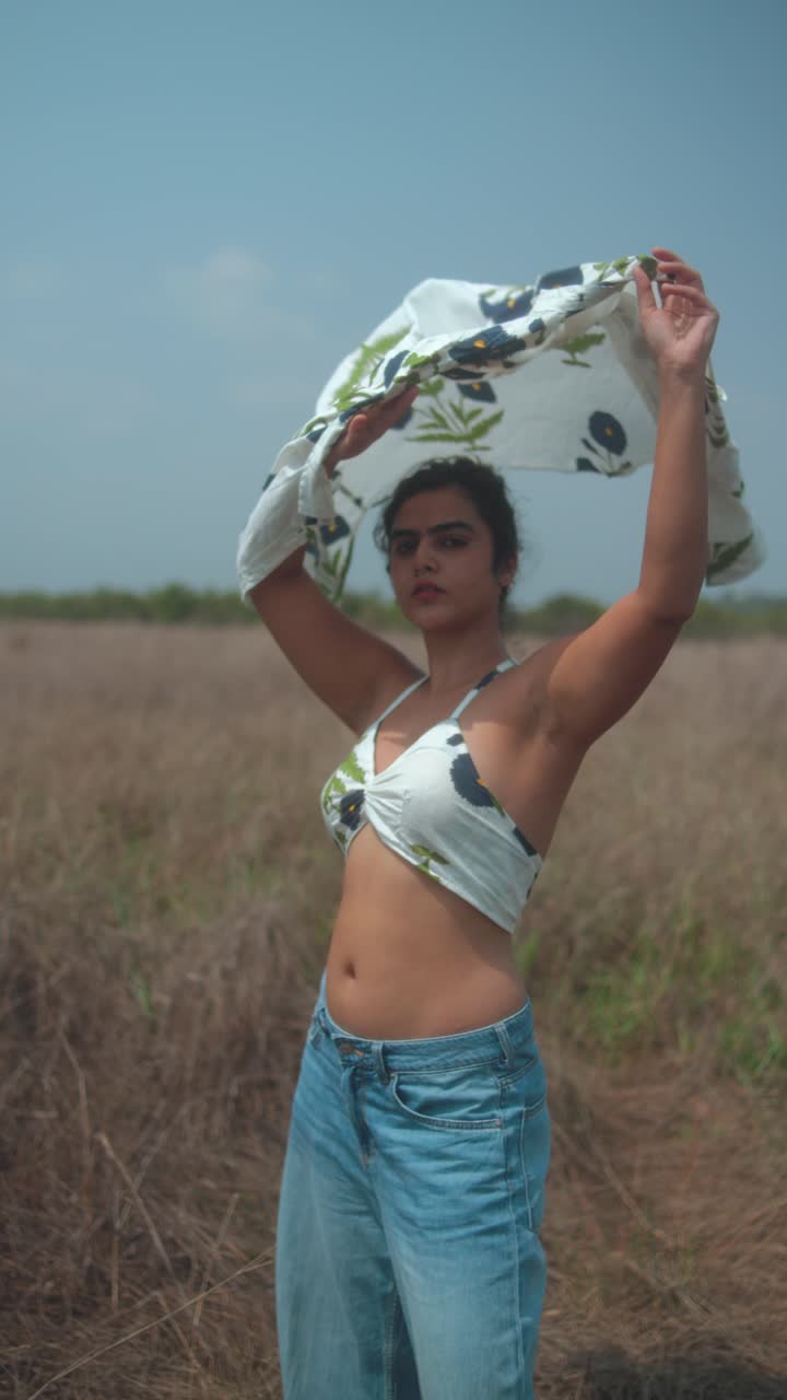 Young woman dancing in a field, holding up a scarf, outdoors, summer mood