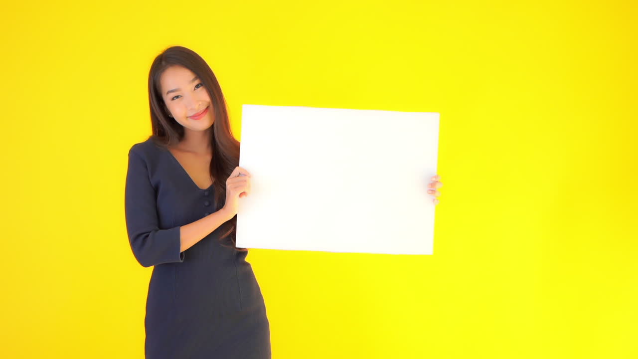 Empty White Board For Motto or Logo Presented by Beautiful Happy Asian Female. Isolated With Yellow Screen Background