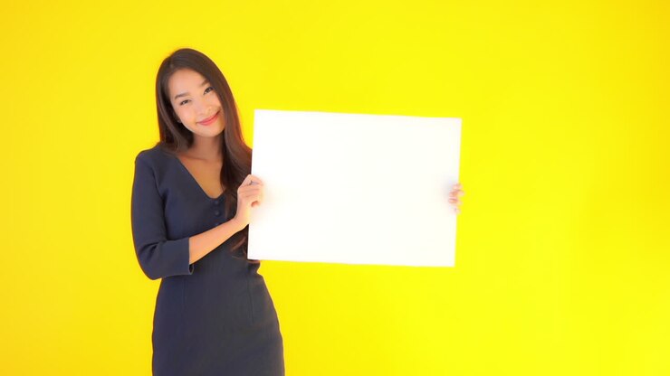 Lavagna bianca vuota per motto o logo presentata da una bellissima e felice donna asiatica. Isolata con sfondo giallo