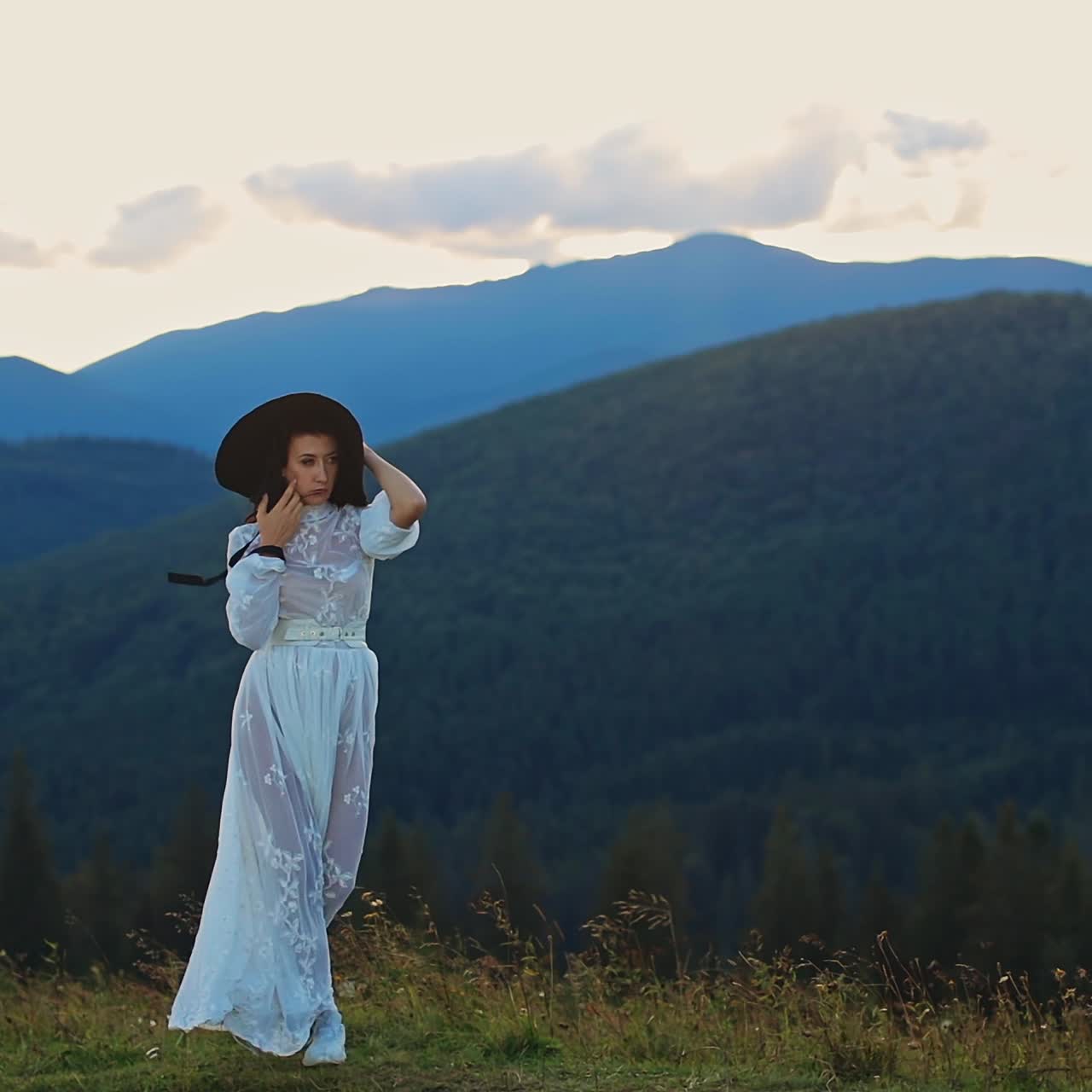 Pretty woman in white dress walking in the mountains. Beautiful female model on green landscapes