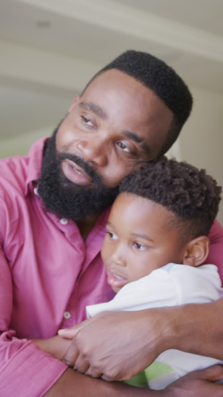 Video verticale di padre e figlio afroamericani seduti sul divano che si abbracciano, al rallentatore