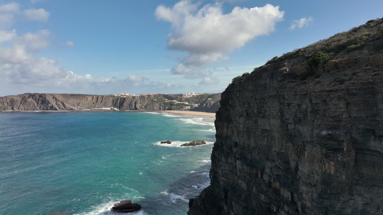 Ripresa aerea rivelatrice che sorvola una scogliera assolata verso una splendida baia sotto un cielo blu